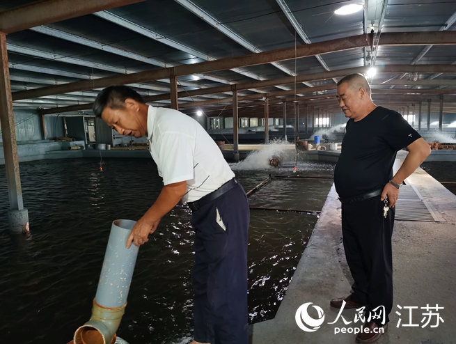 沈玉華（右）在溫室大棚內(nèi)為村民講解鰻魚養(yǎng)殖過程中的細(xì)節(jié)。人民網(wǎng)記者王繼亮攝